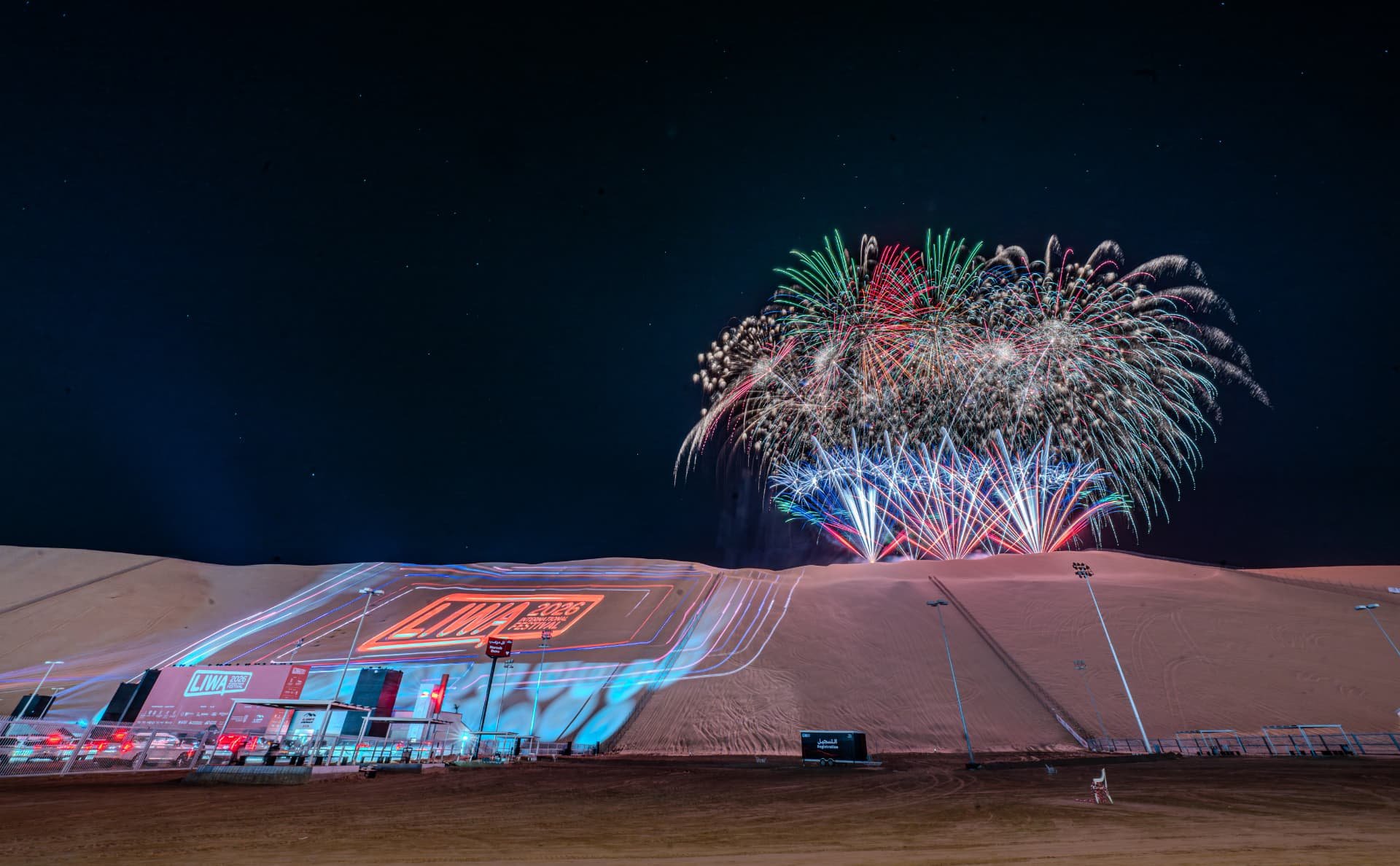 Illuminated Liwa Festival hillside beneath a night fireworks display